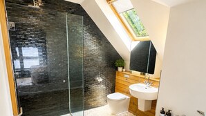 Une salle de bain moderne dotée d’une douche à parois de verre, d’une baignoire sur pieds, de toilettes blanches et d’un meuble-lavabo en bois avec un vasque.