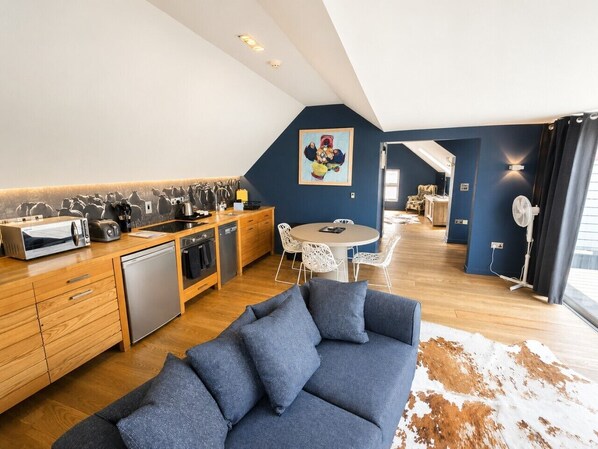 Une cuisine moderne avec des meubles en bois, un coin repas avec une table ronde et des chaises, et un salon avec un canapé bleu.