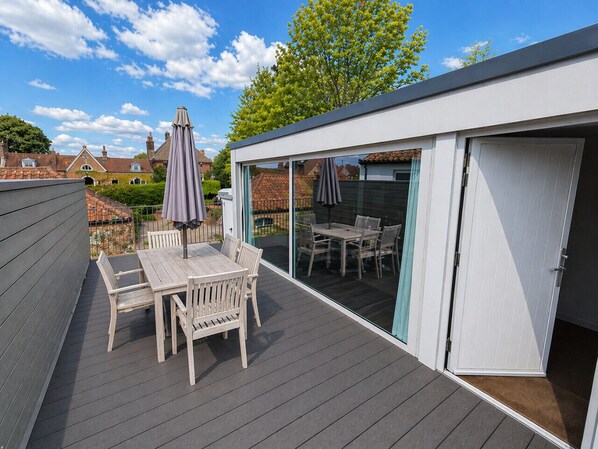 A deck with a table and chairs, a sliding glass door, and a view of a garden. - Print Room 2 at Strattons Hotel (Hingham)
