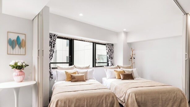 Une chambre d’hôtel moderne avec deux lits, une petite table ronde ornée d’un vase et une fenêtre avec des rideaux à motifs.