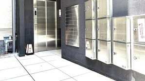 Une entrée d’immeuble avec un ascenseur en métal, un système d’alarme incendie et un panneau indiquant les numéros des pièces.