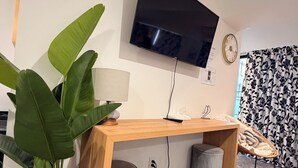 Une chambre moderne avec un bureau en bois, un téléviseur fixé au mur, une plante en pot, une horloge et un rideau à motifs.