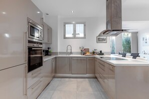 A modern kitchen with stainless steel appliances, a large window, and a view of greenery outside. - Spacious 80m² Cannes Apt with Huge Terrace (Cannes)