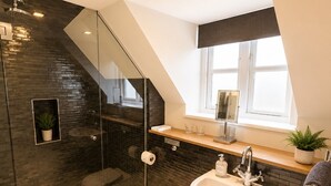 A modern bathroom with a glass shower enclosure, a white toilet, a sink with a mirror, and a window above the sink.