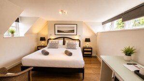A bedroom with a bed, two bedside tables, a desk, a chair, and a window.