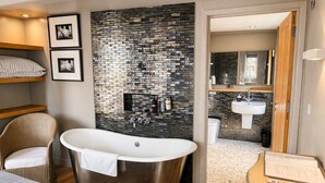 A modern bathroom with a freestanding bathtub, a wicker chair, and a visible shower area. - Cocoes ONE King Apartment at Strattons (Swaffham)