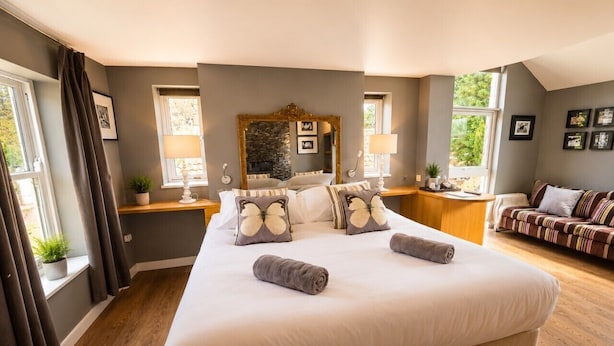 A large bed with two pillows, a bedside table, a mirror, and a window with curtains. - Cocoes ONE King Apartment at Strattons (Swaffham)