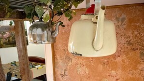 A dining area with a rustic wooden table, chairs, a vase with feathers, a wall-mounted light fixture, and a hanging plant. - Gite "La Greniette (Châteauneuf-sur-Loire)