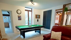 A living room with a pool table, a red sofa, a coffee table with flowers, and a door leading to another room. - Gite "La Greniette (Châteauneuf-sur-Loire)