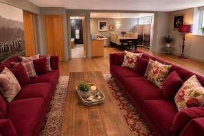 Ein Wohnzimmer mit zwei roten Sofas, einem Couchtisch mit Pflanze und Kerze sowie einem Essbereich mit Tisch und Stühlen.