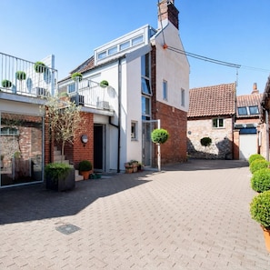 Ein Wohngebäude mit modernem Design, mit Balkon, Garage und einem gepflasterten Innenhof.
