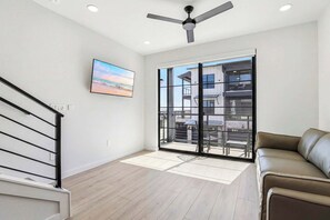Un salon moderne avec un balcon, un ventilateur de plafond et une grande fenêtre.