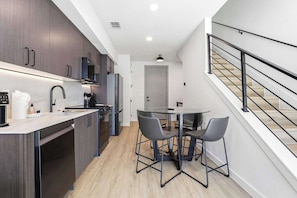 A modern kitchen with dark wood cabinets, a stainless steel sink, and a dining area with two chairs.
