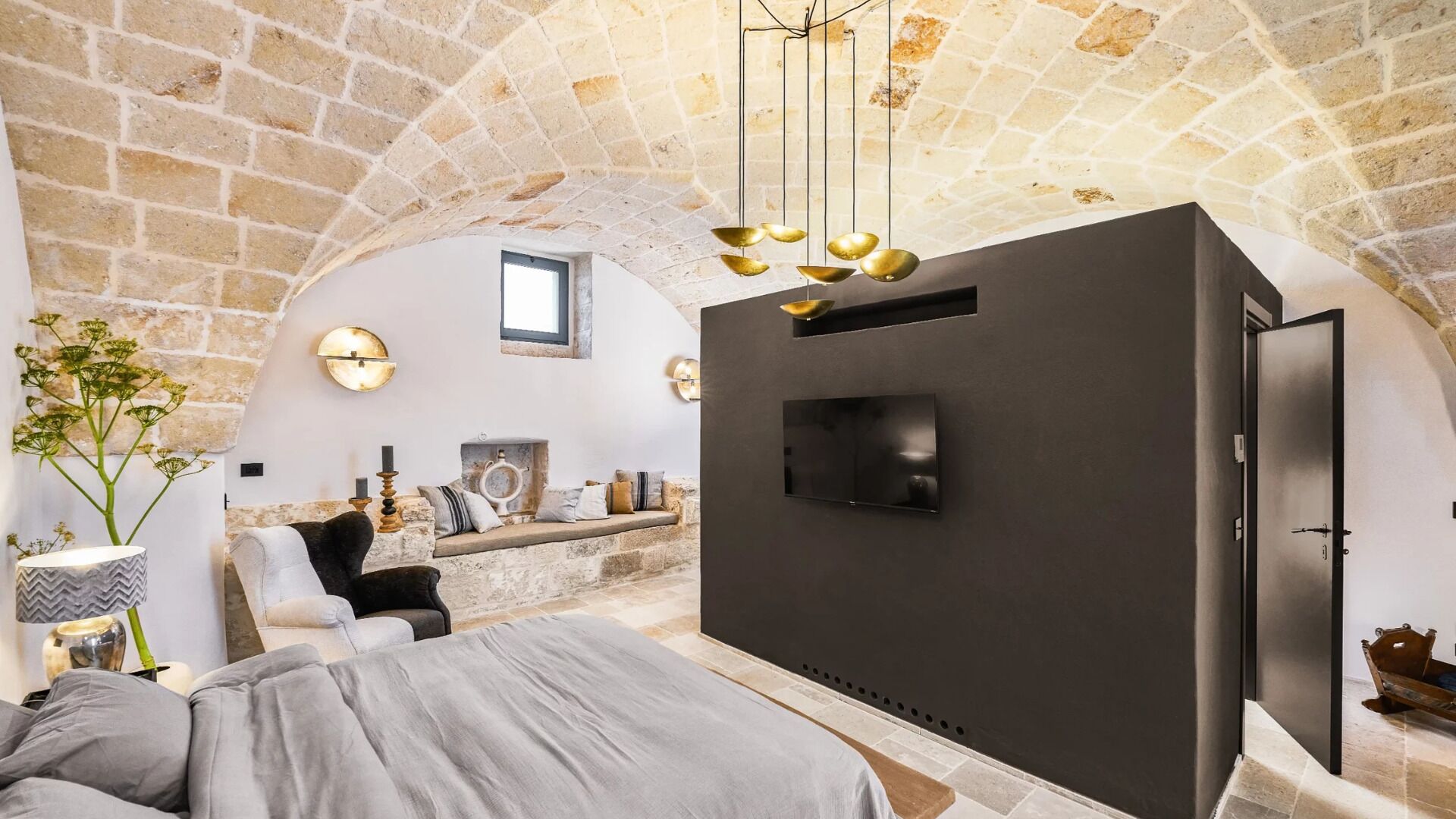 Ein gemütliches Zimmer mit Steindecke, einem Bett, einem Kamin und einem an der Wand befestigten Fernseher.