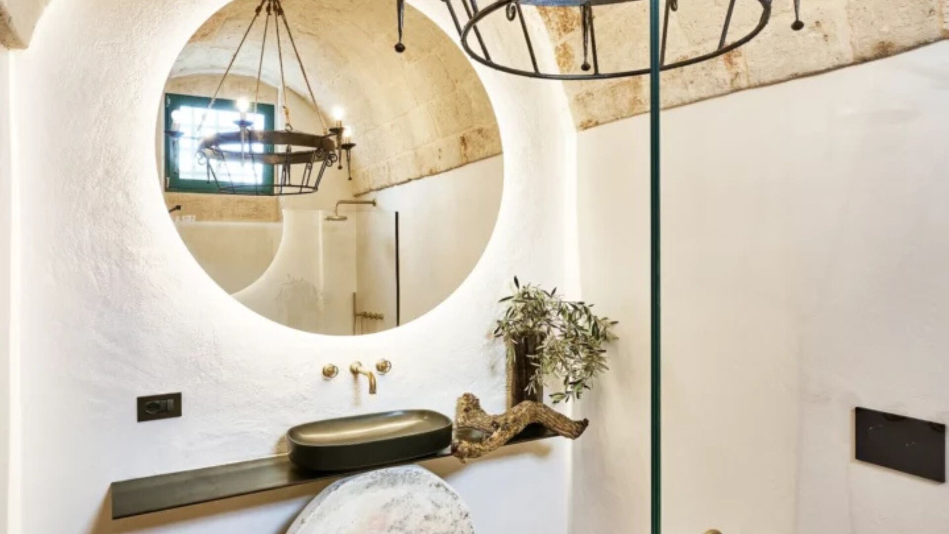 A bathroom with a round mirror, a sink, a plant, and a rustic ceiling.