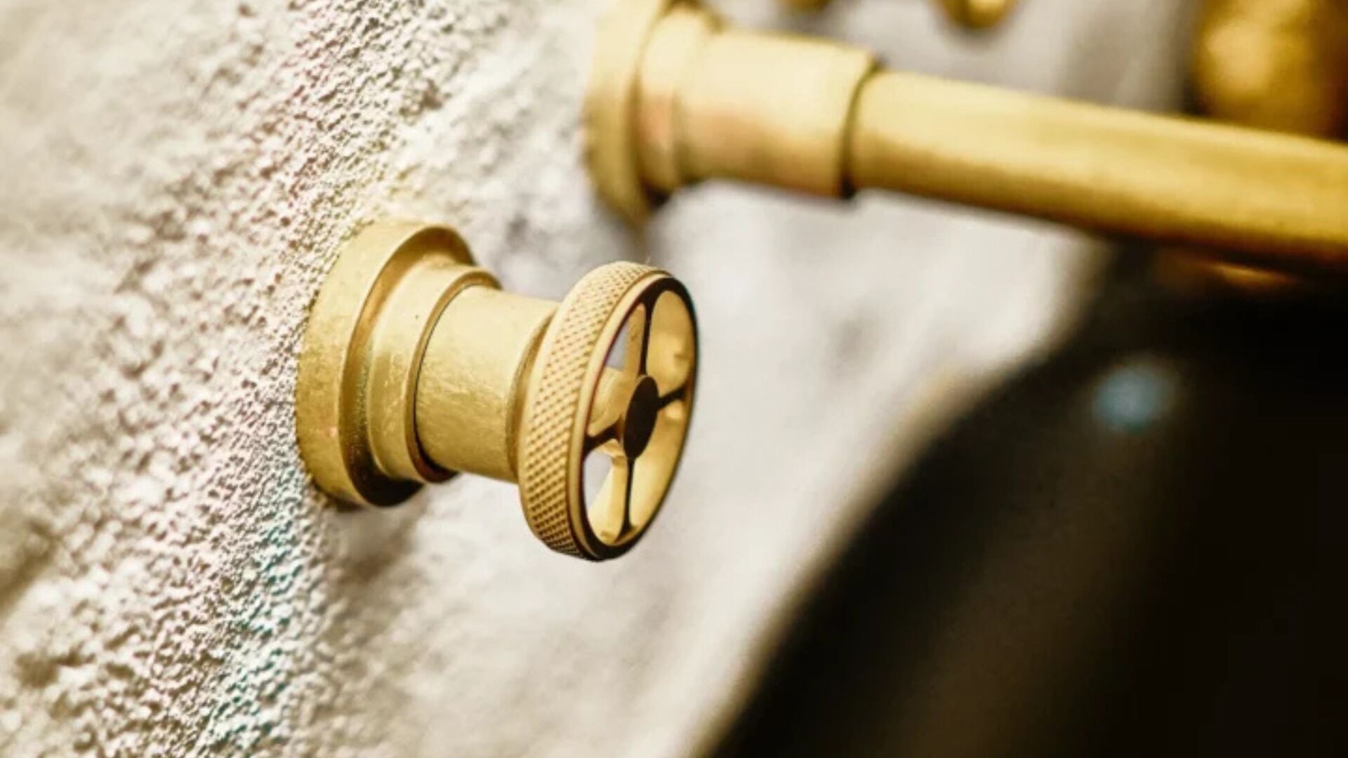 A brass faucet with a lever handle attached to a textured wall.
