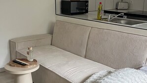 Un saló amb un sofà, una taula rodona petita i una cuina amb armaris i electrodomèstics.