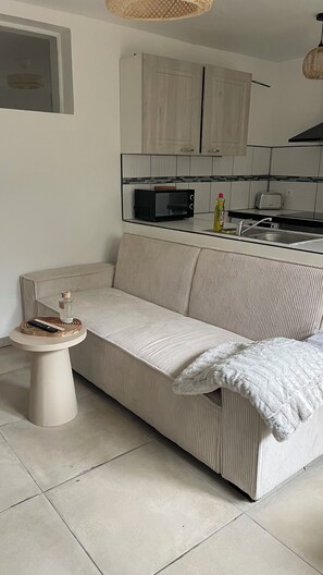 A living room with a sofa, a small round table, and a kitchen area with cabinets and appliances. - Apartment Design Private Terrace Comfort & Serenity (Les Pennes-Mirabeau)