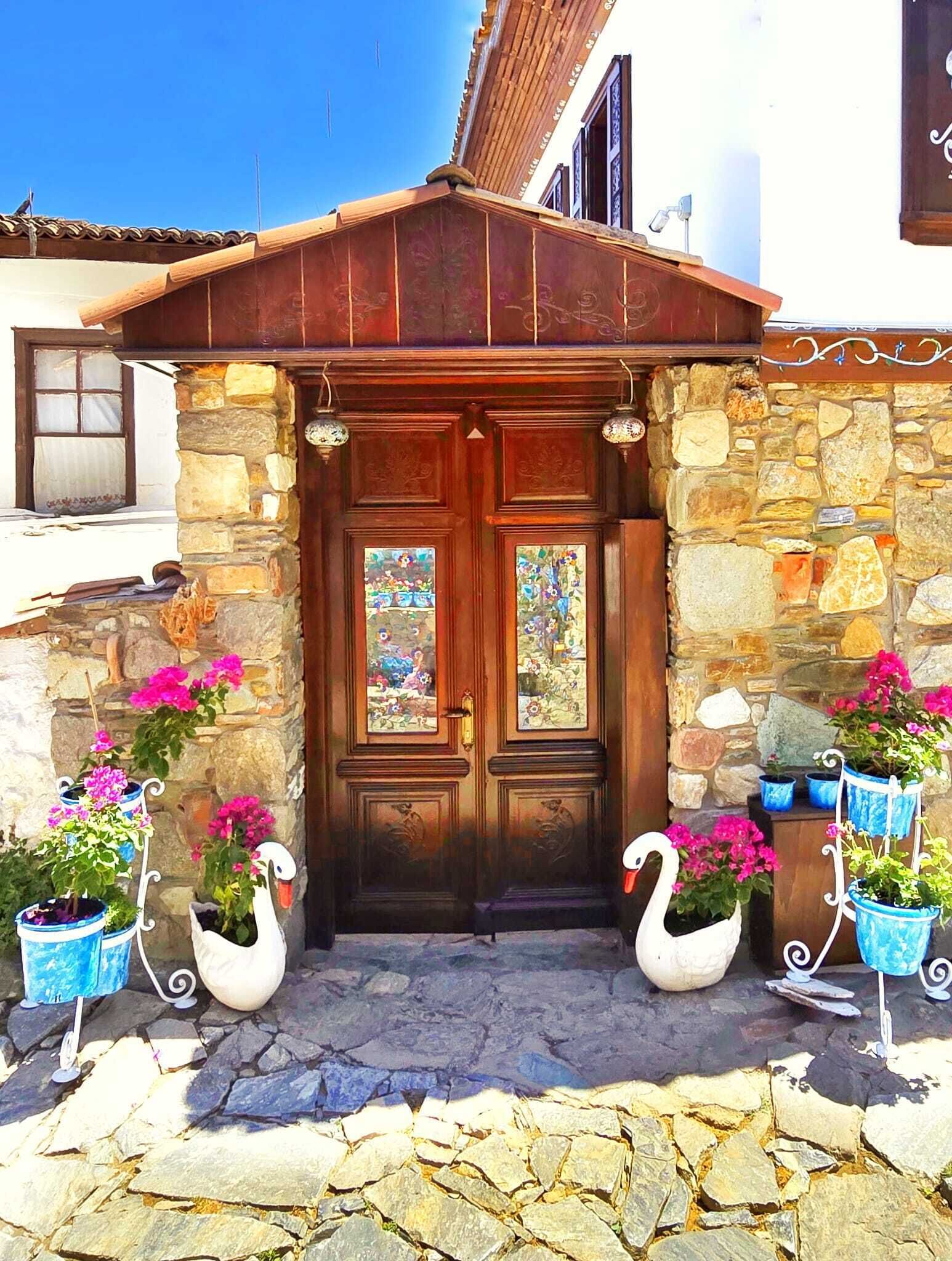 A stone facade with a wooden door, two windows with stained glass, and decorative swans with potted flowers.