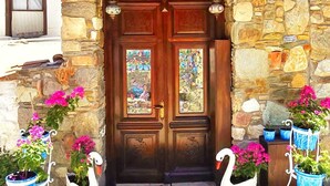 A stone facade with a wooden door, two windows with stained glass, and decorative swans with potted flowers. - Sirincem Plus (Selcuk)