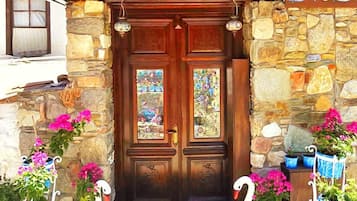 A stone facade with a wooden door, two windows with stained glass, and decorative swans with potted flowers.