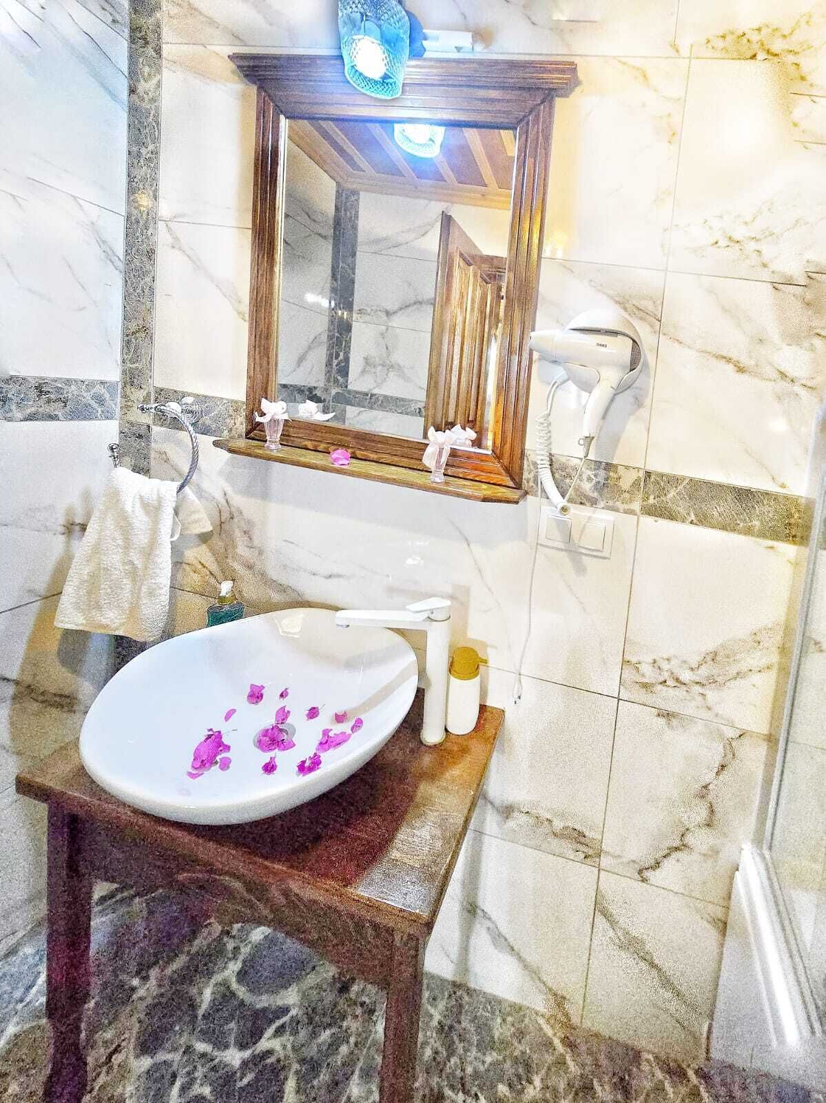 A bathroom with a marble sink, a wooden vanity, a mirror, and a towel rack.