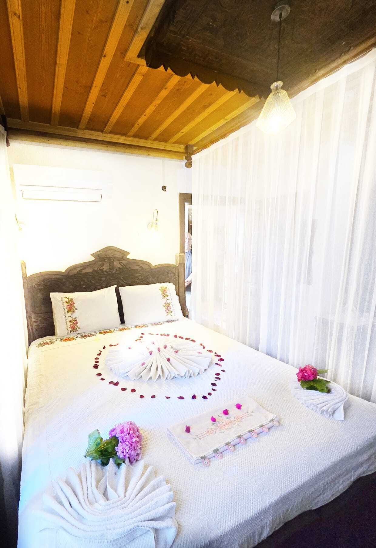 A neatly made bed with floral pillows, a decorative towel arrangement, and a small bedside table with a book and flowers.