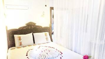 A neatly made bed with floral pillows, a decorative towel arrangement, and a small bedside table with a book and flowers.