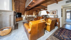 A spacious living room with a high ceiling, wooden beams, leather sofas, a fireplace, and a television. - Innsbrook Vacation Townhome 57 (Ruidoso)