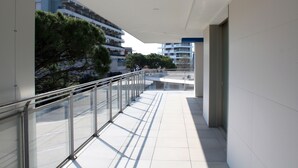 A modern building with a glass balcony, white tiled floors, and a view of other buildings and trees. - Stylish Flat in Piazza Fontana (Lignano Sabbiadoro)