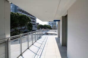 A modern building with a glass balcony, white tiled floors, and a view of other buildings and trees. - Stylish Flat in Piazza Fontana (Lignano Sabbiadoro)