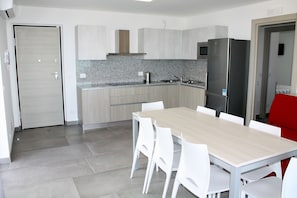 Cozinha moderna com mesa de madeira, cadeiras brancas, geladeira e micro-ondas.