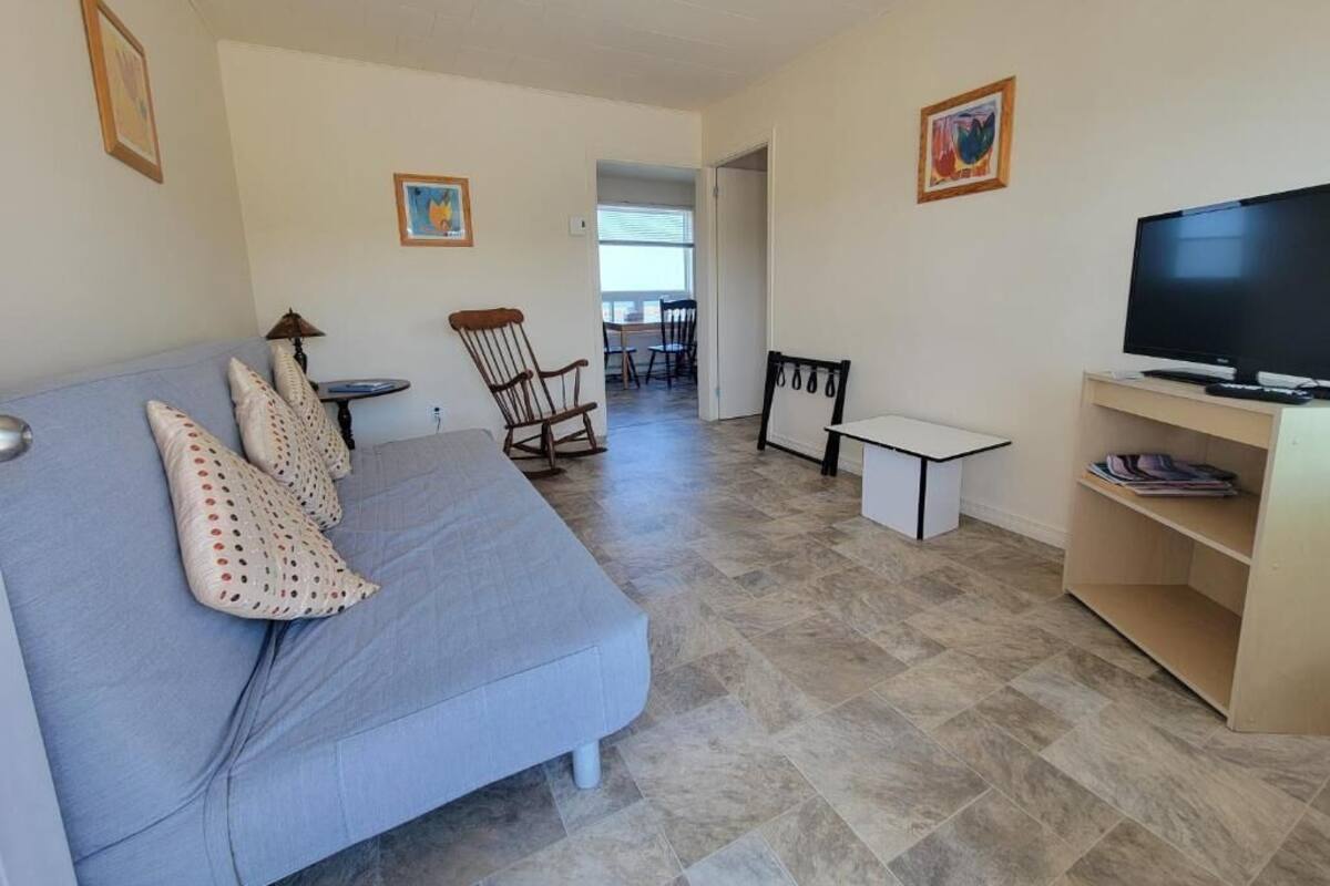 Una sala de estar con un sofá, un mueble para televisión y un rincón de comedor al fondo.