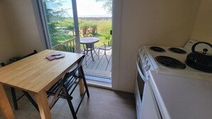 Een keuken met een fornuis, een eettafel met stoelen en een schuifdeur naar een terras buiten met een tafel en stoelen.