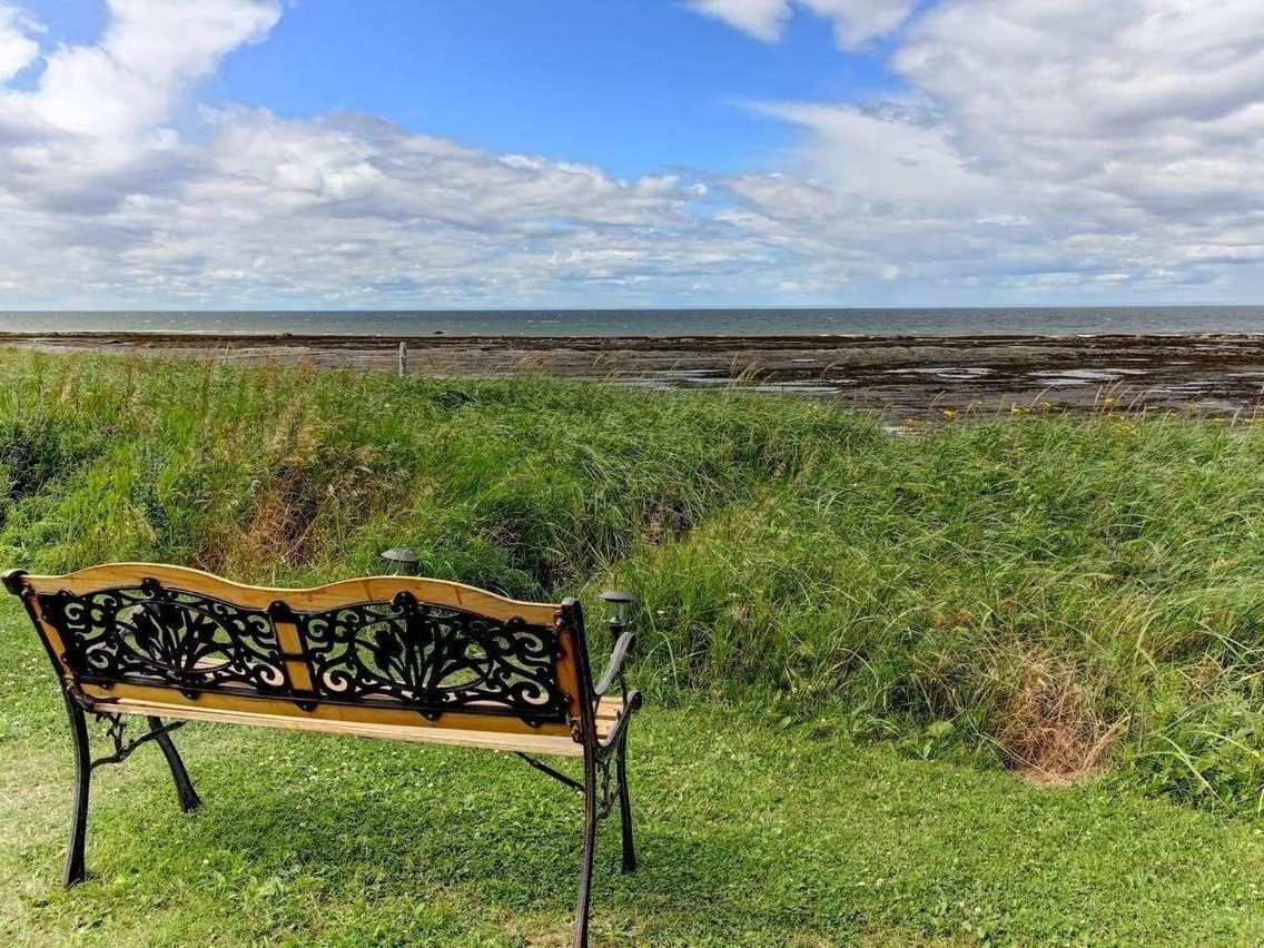 Eine Bank mit aufwendiger Metallverzierung, auf einer Rasenfläche mit Blick auf das Meer und den Himmel.