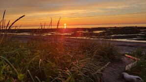 Een zonsondergang boven een strand, met gras op de voorgrond.