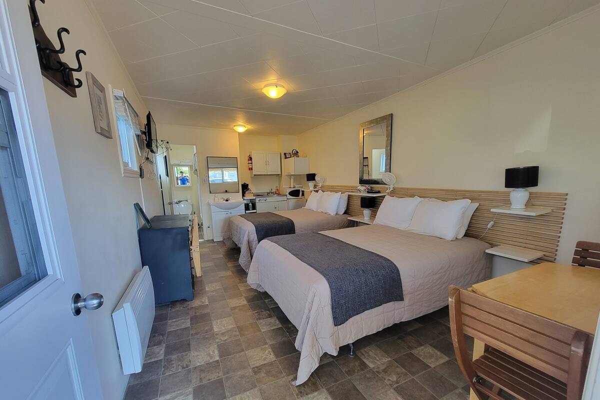 Habitación de hotel con dos camas, una mesita, una silla, baño y kitchenette.
