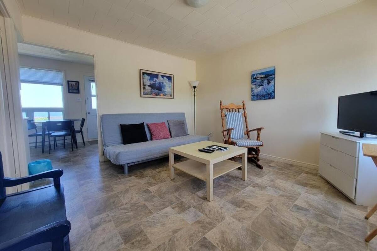 Una sala de estar con un sofá, un sillón mecededor, una mesa de centro, un mueble para la televisión y un comedor con sillas y una mesa.