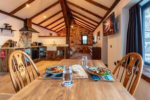 Une cuisine rustique aux murs de pierre, avec des poutres en bois et une table à manger dressée avec des assiettes et des verres.