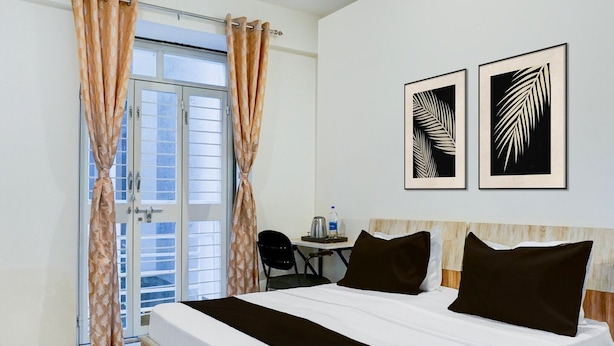 Una habitación de hotel con cama, escritorio, dos obras de arte con hojas enmarcadas y vistas a través de una puerta de cristal.