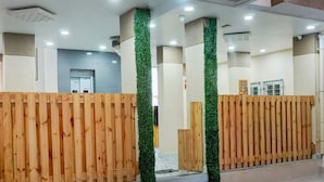 Un área de recepción con separadores de madera, detalles verticales verdes y piso de baldosas.