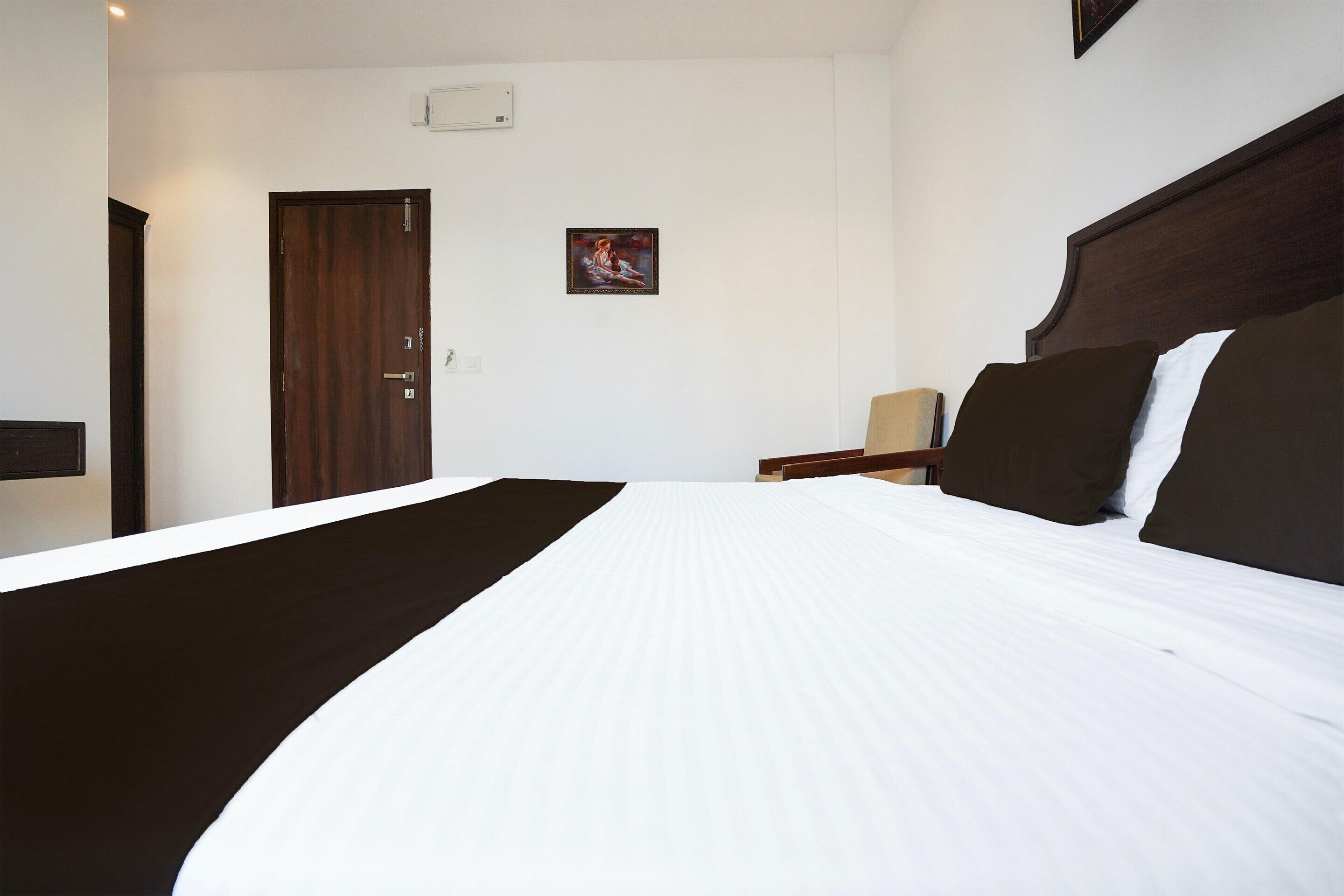 A hotel room with a large bed, a wooden door, a small table with a lamp, and a framed picture on the wall.