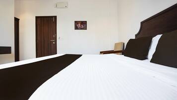 A hotel room with a large bed, a wooden door, a small table with a lamp, and a framed picture on the wall.