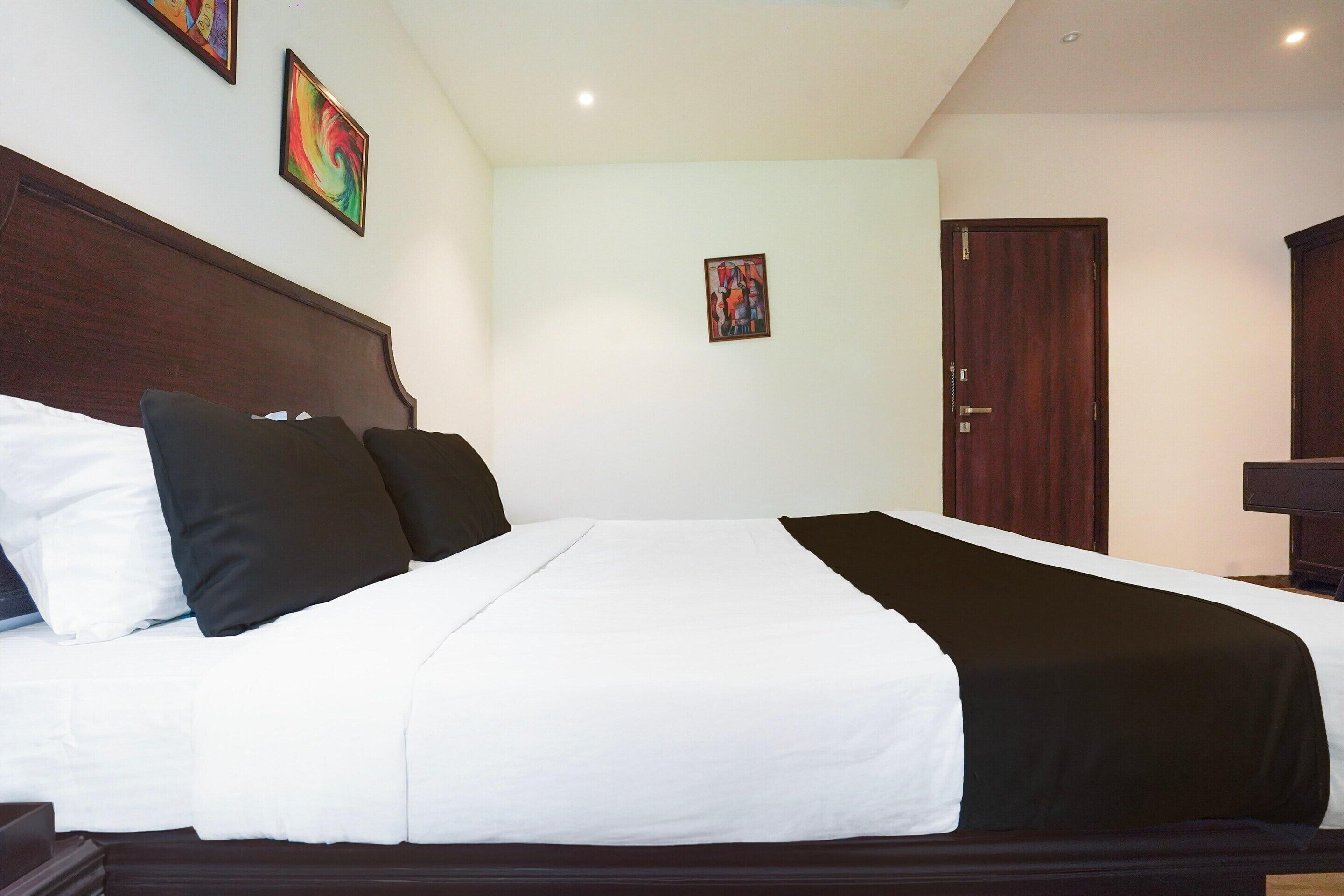 Une chambre d’hôtel avec un grand lit, une tête de lit en bois, deux tableaux au mur et une porte sur le côté droit.