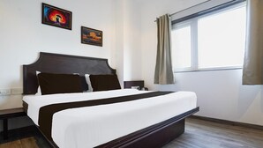 A hotel room with a large bed, a window with curtains, and two framed pictures on the wall. - Super Deluxe Octave Parkland Suites (Nagpur)