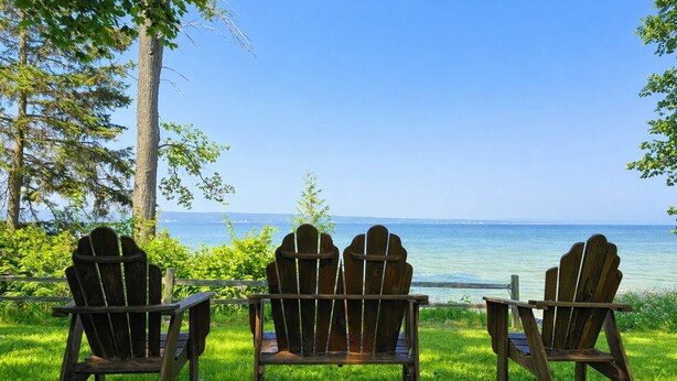 Drei hölzerne Adirondack-Stühle mit Blick auf ein Gewässer, bewölkter Himmel.