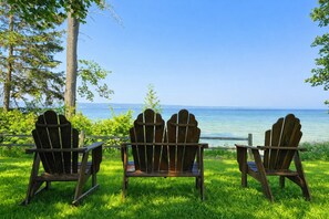 Three wooden Adirondack chairs facing a body of water with a clear sky. - Waterfront Burt Lake Cottage | Sleeps 6 (Indian River)
