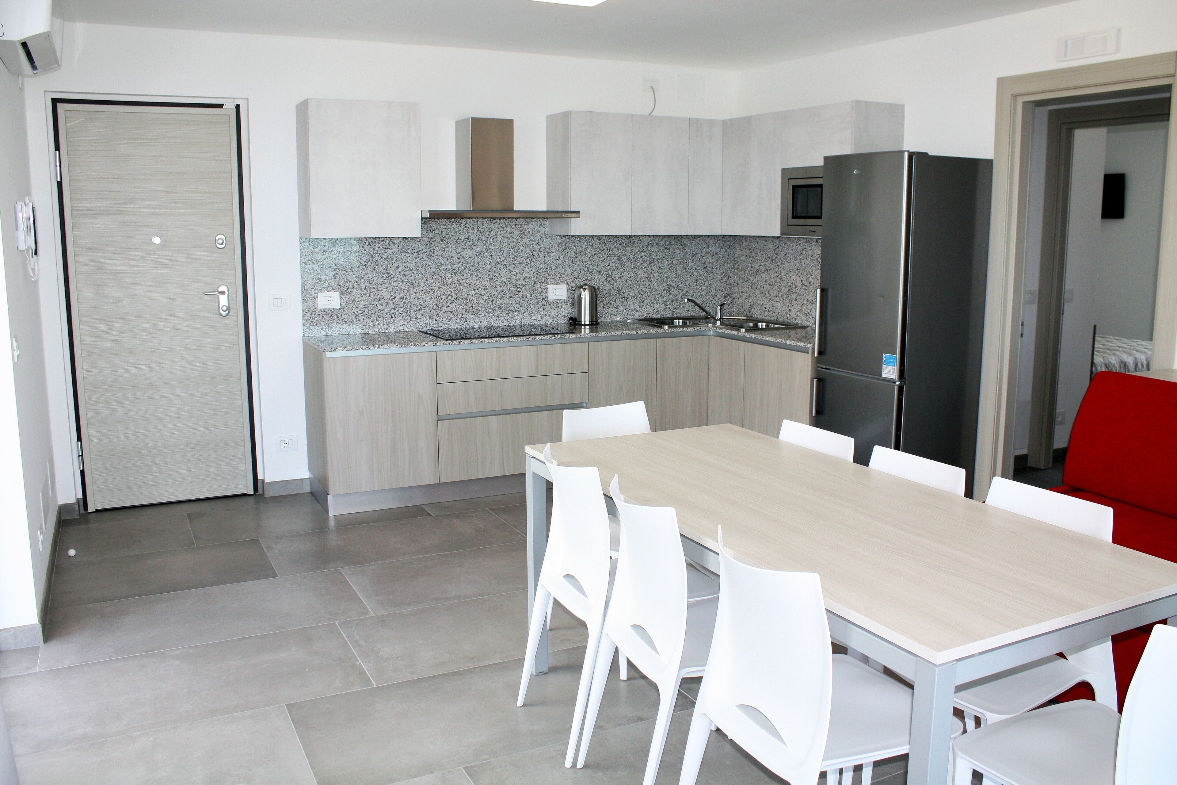 A modern kitchen with a wooden table and white chairs, a refrigerator, and a microwave.