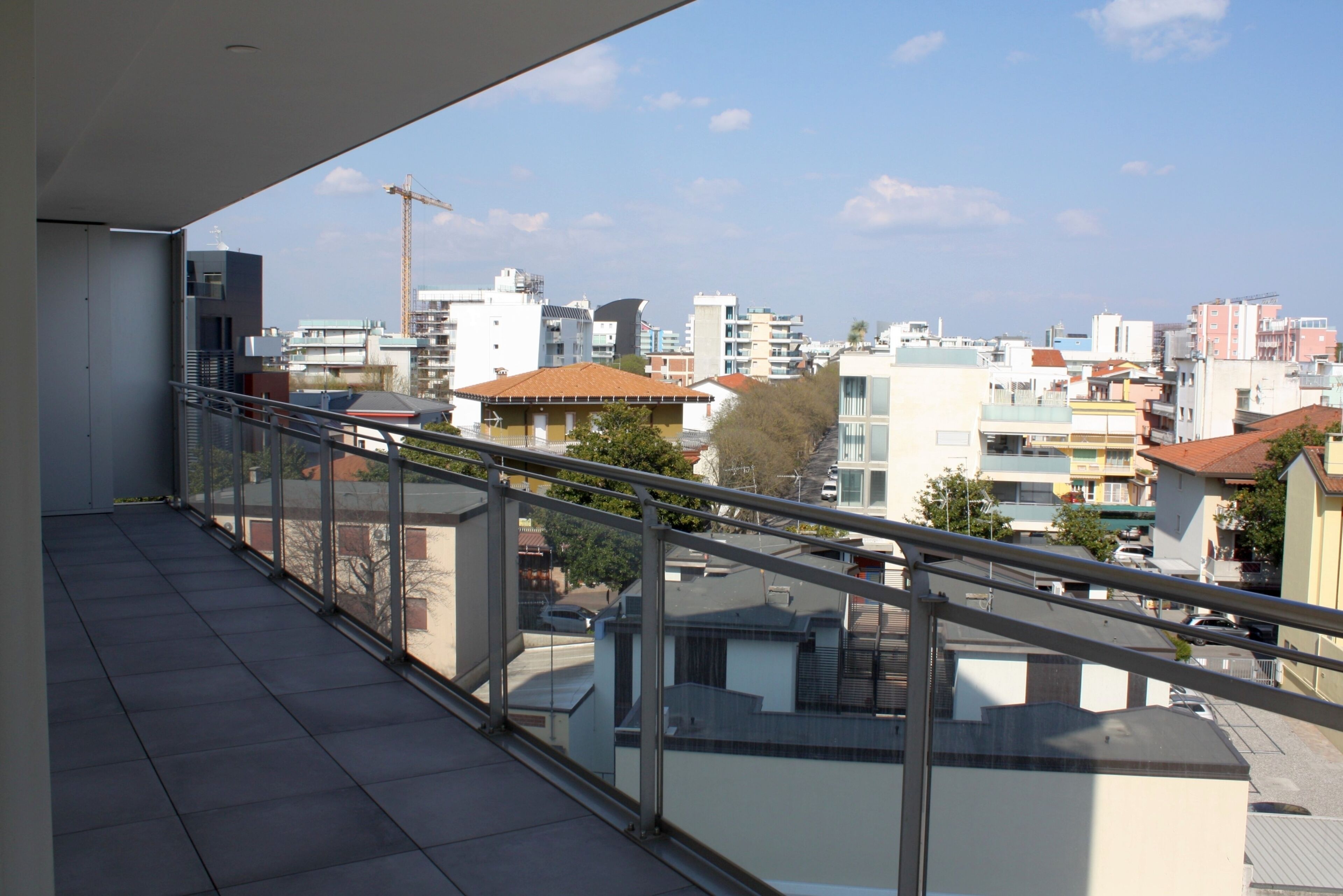 A balcony with a metal railing overlooking a cityscape with various buildings and a construction crane in the distance.