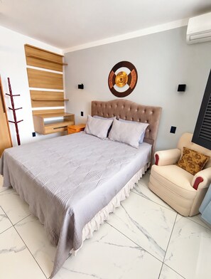 A bedroom with a large bed, a chair, a wall-mounted shelf, and a decorative wall piece. - Vacation home with a pool, 150 m from the beach in Piratininga (Niterói)